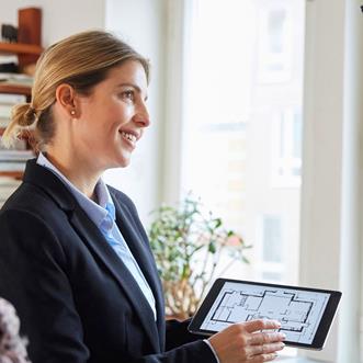 En kvinnlig mäklare står med en ipad och visar en planlösning