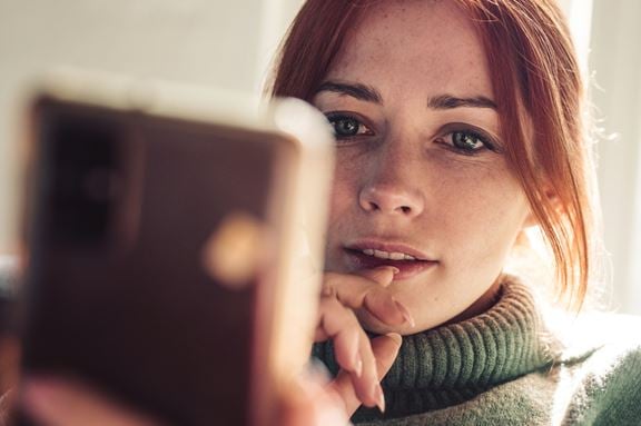 Rödhårig tjej som sitter med sin telefon i handen