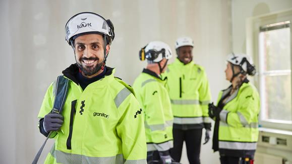 Fyra elektriker iförda varselkläder, varav en ler mot kameran medan övriga pratar med varandra i bakgrunden.