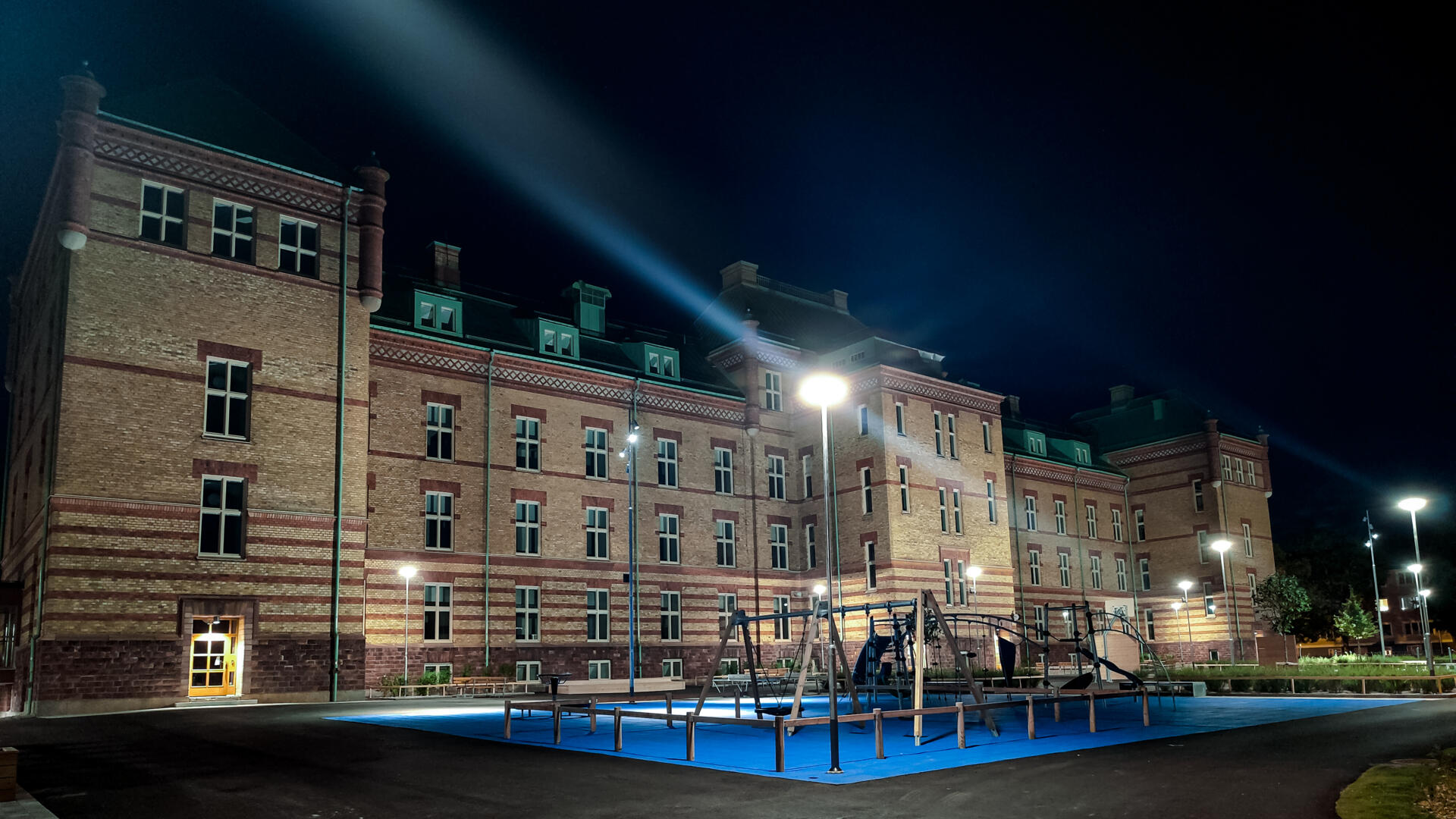 Den betong- och glasförsedda fasaden av gamla skatteskrapan sträcker sig upp mot en blå himmel. Längst ner syns den färgsprakande skylten som lyder "skrapan".