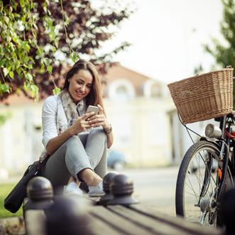 En tjej sitter på en parkbänk och kollar i sin mobil
