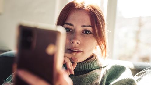 Rödhårig tjej som sitter med sin telefon i handen