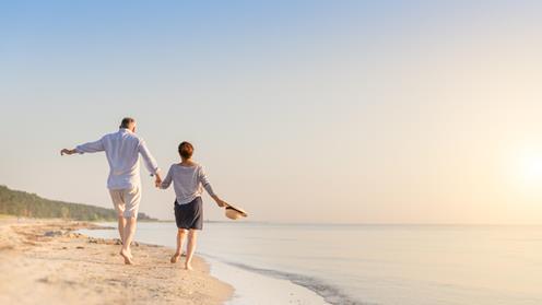 Ett äldre par går hand i hand på stranden