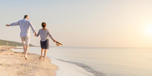 En kvinna och en man går hand i hand på en strand