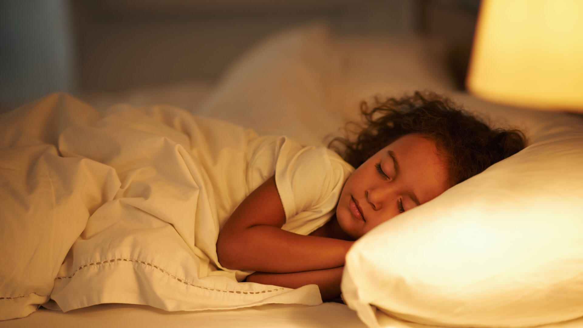 Flicka sover gott i sin säng i svagt ljus.