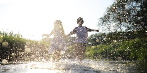 Pojke och flicka springer genom en vattenpöl