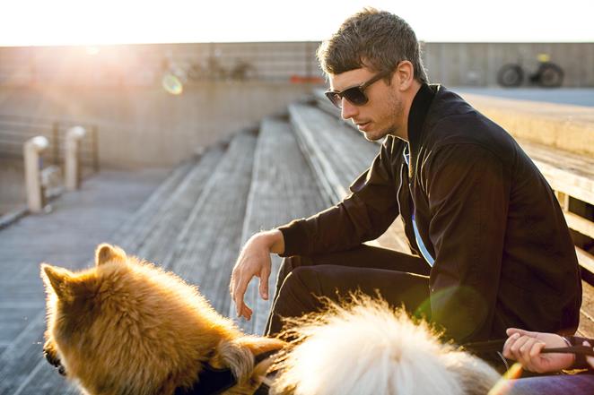 Man med solglasögon sitter vid en kaj tillsammans med sin hund