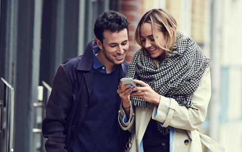 En man och en kvinna som går på en gata och kollar ner i en mobil