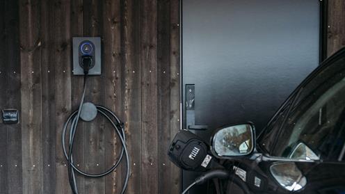 Laddaren Zaptec Go mot en trävägg och med en laddkabel inkopplad till en bil